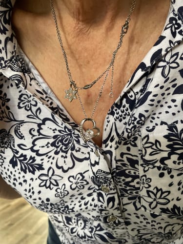 A customer wearing the silver-colored forever love necklace with its heart-shaped pendant, layered with another necklace.