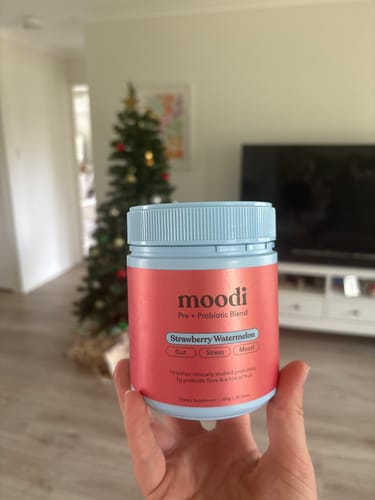 Customer holding a tub of Strawberry Watermelon pre and probiotic blend in a home with a Christmas tree.