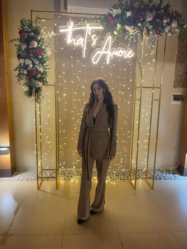 Cliente indossa il tailleur Parigi gessato beige a un evento, con il blazer cinturato e i pantaloni a gamba larga.