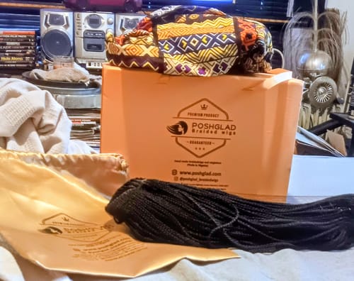 Customer's unboxed black Cornrow Braids wig laid out next to its orange Poshglad box and golden satin bag.