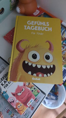 Ein Kunde zeigt das gelbe Gefühlstagebuch für Kinder auf einem Tisch.