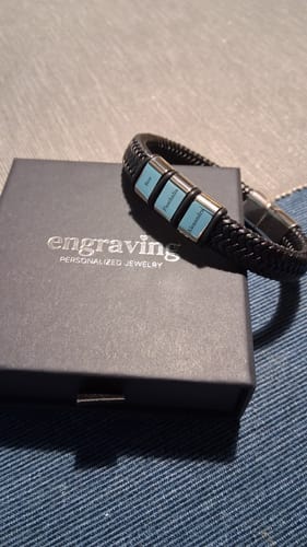 Customer's black braided Viking bracelet with three personalized silver and turquoise beads, shown on its black jewelry box.