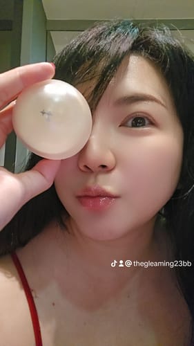 Reviewer holding the round Super Peptide Overnight Lip Mask container over one eye, with soft, hydrated lips.