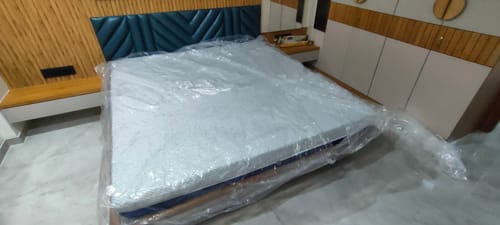 Customer's new Flo Anti-Gravity™ Latex Mattress in its plastic wrap, shown from an angle on a bed frame.