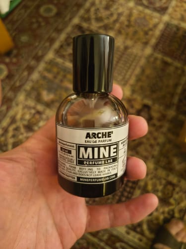 Un cliente tiene in mano la boccetta del profumo ARCHÉ, mostrando l'etichetta bianca.