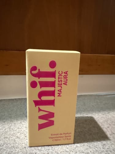 Customer's Majestic Aura perfume box, cream-colored with bold pink lettering, on a counter.