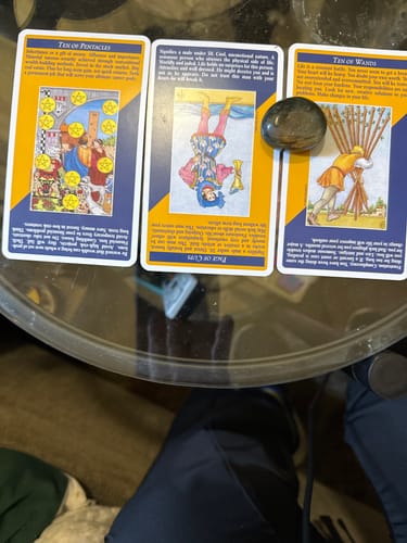 Customer's polished dark crystal resting on three tarot cards on a glass table.