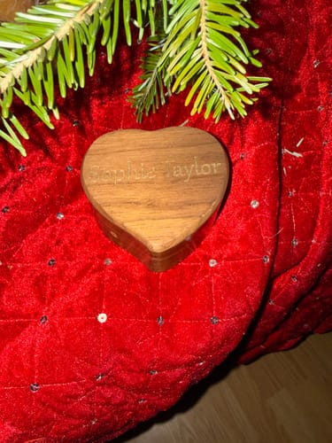Customer's heart-shaped wooden Wind-up Music Box with a name engraved on top, resting on red fabric.