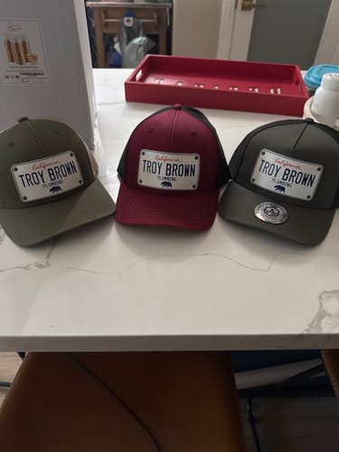 Customer's three customized California White Plate Hats in olive, maroon, and dark green on a tabletop.