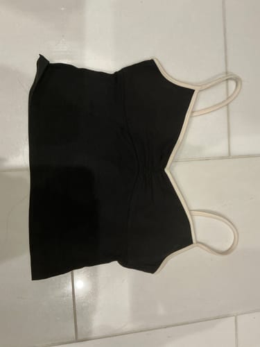 Customer's black Ballet Tank with cream trim and straps, laid flat on a white tiled floor.