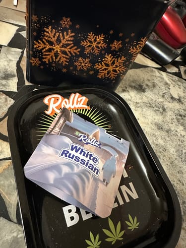 Customer's packaging for White Russian THCA FLOWER on a black rolling tray with a bag in the background.