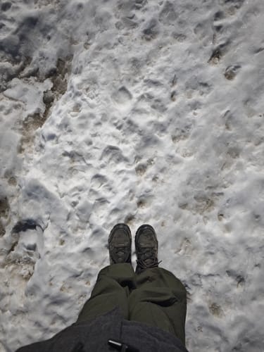 A reviewer's first-person view of their Bacca Bucci Flame boots while standing on a snowy trail.