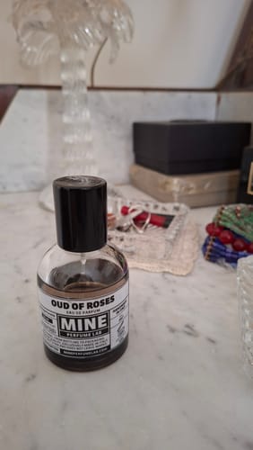 Recensore mostra il flacone di profumo OUD OF ROSES su un ripiano di marmo.