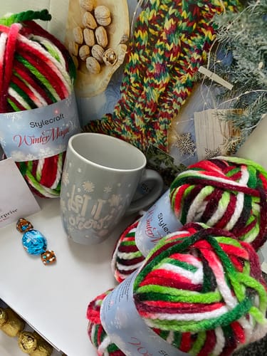 Reviewer's December Special Edition Stocking Box with festive yarn, a grey mug, and two small chocolates.