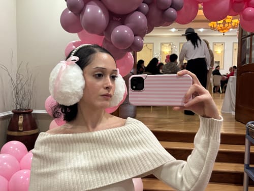 Customer takes a selfie wearing the white furry earmuffs with a pink bow and pearl headband.
