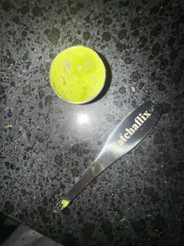 Cliente muestra el polvo verde de Té Matcha Ceremonial en un cuenco medidor junto a una cuchara a juego.