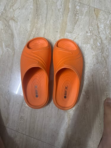 Reviewer's pair of bright orange Bacca Bucci Floats slides on a tiled floor.