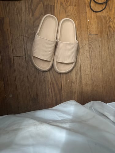 Customer's beige Cloudies slippers with a thick sole, resting on a wooden floor.