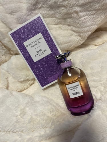 Customer's Coach Dreams Moonlight perfume bottle and its purple glittery box on a fluffy blanket.