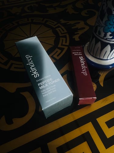Reviewer's packaging for the Skindeep Peptide Lip Glaze and Peptide Milk Toner on a patterned surface.
