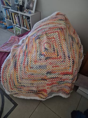 Customer's finished Hearthside Rainbow Blanket, draped in a room. The colorful crocheted blanket features a fluffy white border.