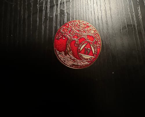 Customer's red and gold 19 Year Sobriety Medallion with a Tree of Life design on a dark surface.