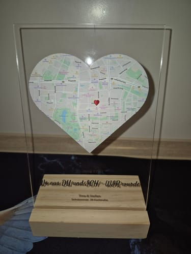 Kunde zeigt die personalisierte Acryltafel „Unser Ereignis“ mit herzförmiger Karte und graviertem Holzsockel.
