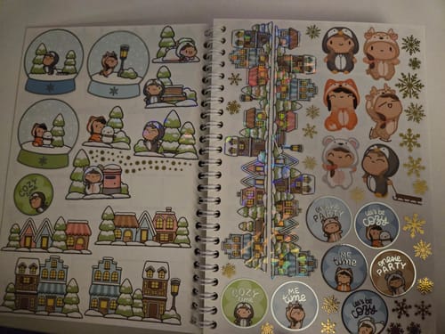 Reviewer shows various sheets from the Winter Onesie Town Sticker Pack, including cute characters and foil designs.