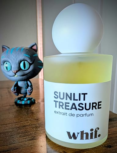 Customer's Sunlit Treasure perfume bottle on a wooden table, next to a whimsical cat figurine.