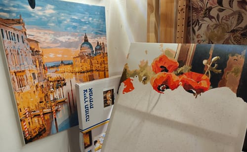 לקוחה מציגה ערכות צביעה לפי מספרים: תמונה גמורה של ונציה ולידה תמונה של פרגים בתהליך צביעה.