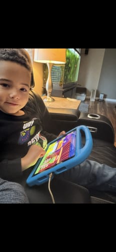 A customer's young child sitting indoors using the First Grade Curriculum on a tablet with a blue case.