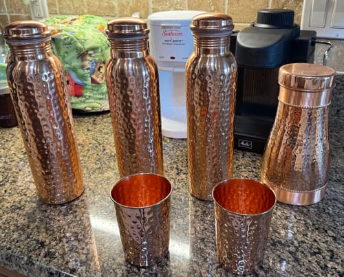 Customer's collection of hand-hammered Pure Copper Water Bottles and matching cups on a kitchen counter.