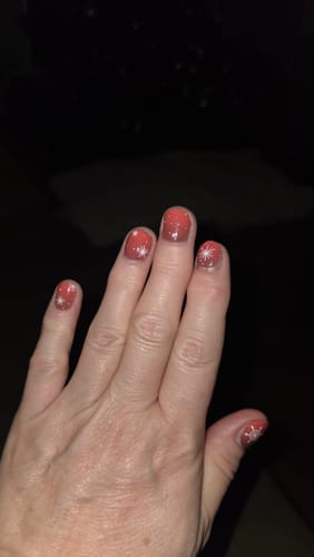 Hand einer Kundin, die ihre Nägel mit den roten „Winter Rouge“ UV-Gelfolien mit Schneeflocken zeigt.