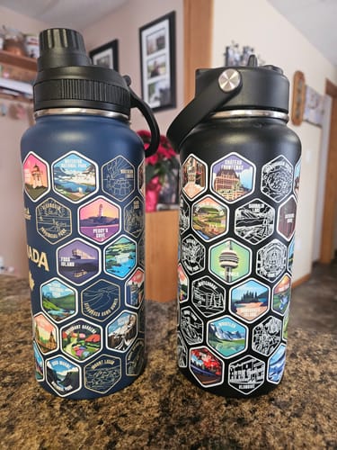 Customer's blue and black Canada Bottles on a countertop, decorated with colorful hexagonal destination stickers.