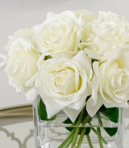 Close-up of a customer's decorative artificial plant, showing white roses arranged in a clear glass vase.