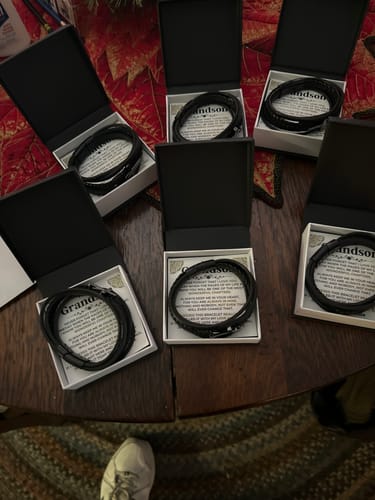 Customer's six Cross Braided Bracelet Gift Sets displayed open in their boxes on a wooden table.