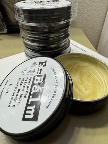 Customer's open tin of F-Balm, showing the yellow balm, next to a stack of three sealed tins.