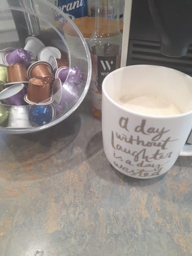 Reviewer's Mocha Blend coffee served in a white mug reading 'a day without laughter is a day wasted' on a counter.