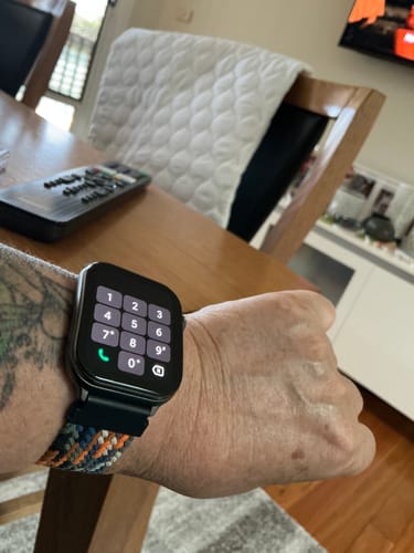 Customer's wrist with a smartwatch showing the phone keypad on the screen, sitting at a wooden table.