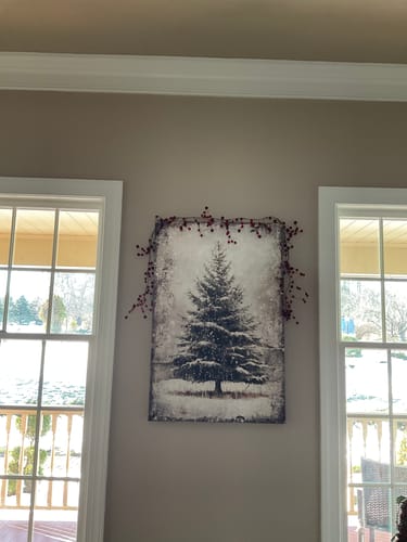Customer's Vintage Pine Tree Christmas wall art hanging on a wall between two windows, decorated with a red berry garland.