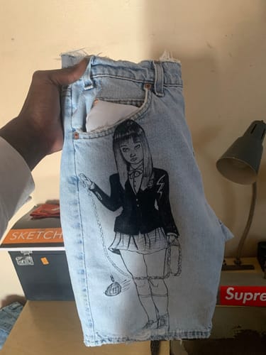 Reviewer holds up a pair of light-wash B Grade Denim Jeans, reworked into shorts with a custom anime-style drawing.