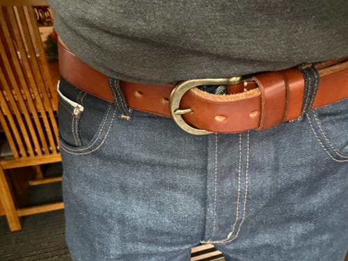 Customer wearing the brown Horseshoe Buckle Leather Belt fastened on a pair of dark blue jeans.