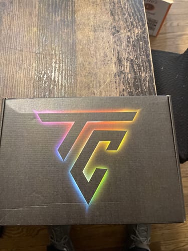 Customer's black TCG89 MYSTERY CASH BOX with a rainbow-colored logo, sitting on a wooden table.