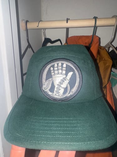 Reviewer's dark green Big Camp Hat with a custom circular patch on the front.
