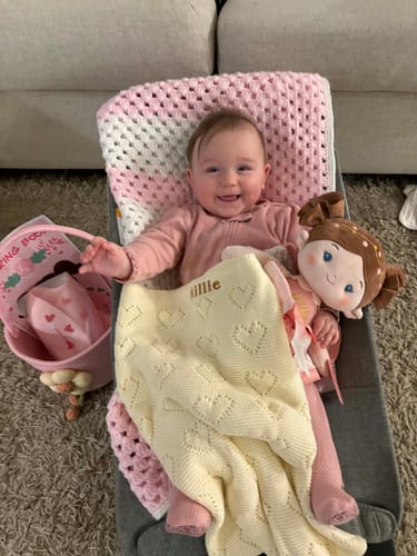 Customer's smiling baby holding the personalized blanket and doll from the Personalized Love Basket.