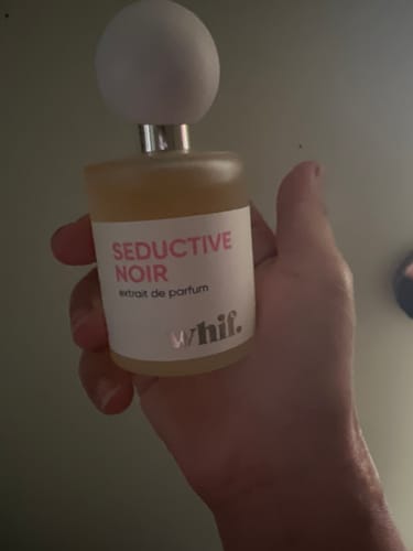 Customer's hand holding the Seductive Noir perfume bottle, showing its white spherical cap.