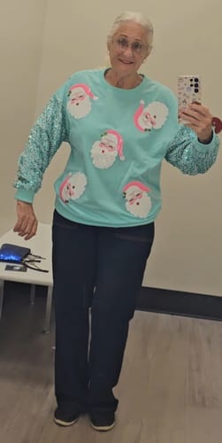 Reviewer trying on the mint green Santa Baby Sweater with sparkly sleeves in a fitting room.