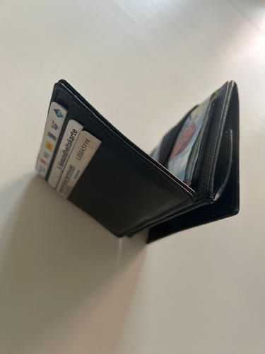 Customer's black Flap Boy wallet, shown open and filled with several cards and banknotes on a white surface.