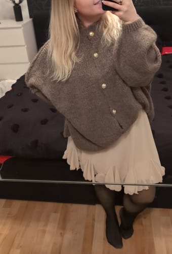 Kundin trägt den braunen Oversized-Cardigan "CozyGlam" und den hellen Rock "Summer" in einem Spiegelselfie.