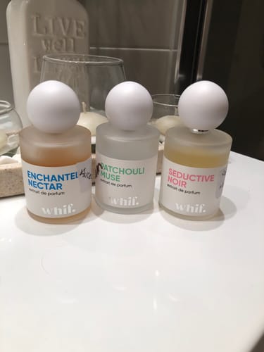 Reviewer's Seductive Noir perfume in a frosted glass bottle, shown with two other fragrances on a white counter.